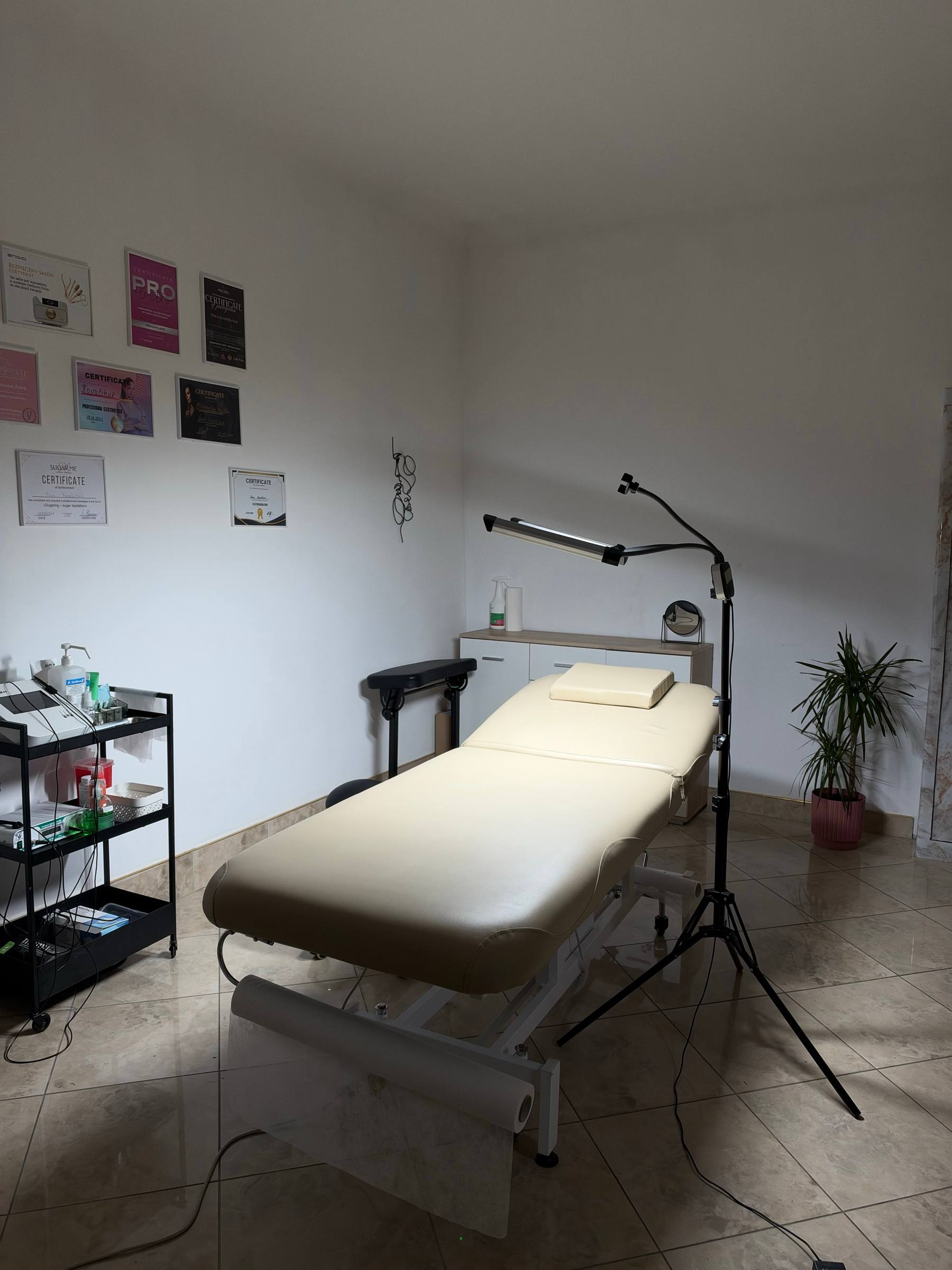 Gabinet Tok Shok Studio: leżanka zabiegowa, lampa, wózek z aparatem i certyfikaty na ścianie